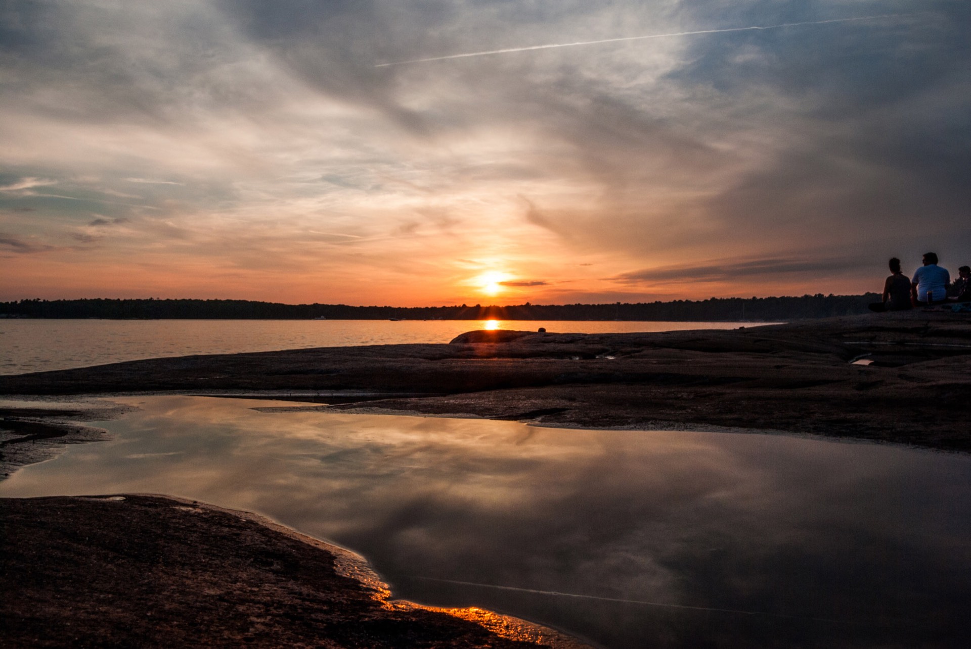 Pink granite shoreline and a calm pool in the rock at sunset, Killbear Provincial Park on Georgian Bay, two people sitting at the water's edge